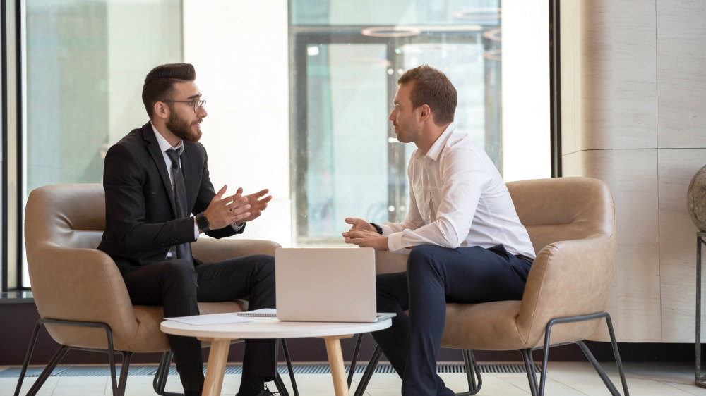 Middle eastern and caucasian ethnicity businessmen seated on armchair in modern office | Salesperson Skills Of Top Performers [INFOGRAPHIC] | sales person skills | sales skills